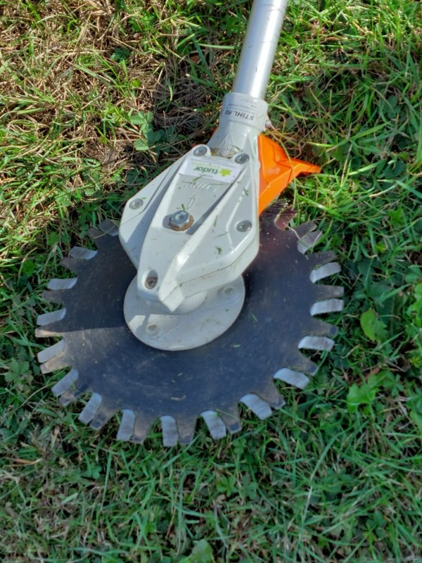 Close-up of a metal cutting blade fitted to a brushcutter, resting on grass