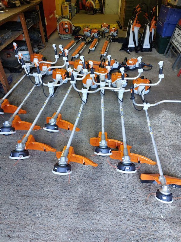 Rows of orange brushcutters and backpack sprayers laid out on a depot workshop floor