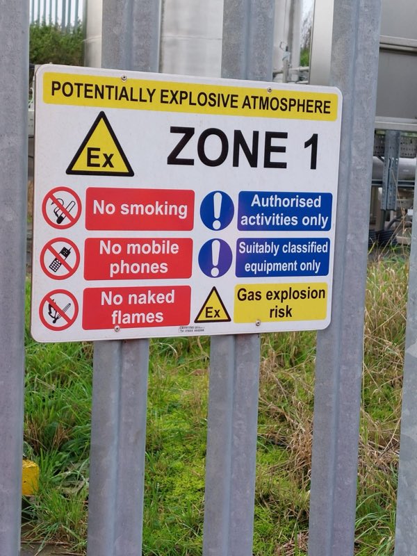 Potentially explosive atmosphere Zone 1 sign fixed to a steel palisade fence, with storage tanks behind