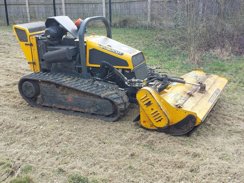 Yellow remote-controlled tracked flail mower parked on rough grass