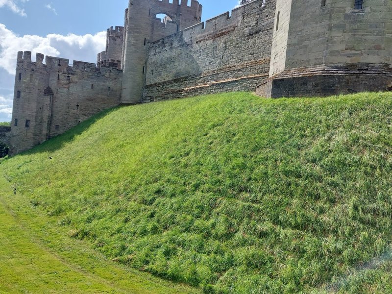 Steep grass bank below a stone castle wall, recently cut